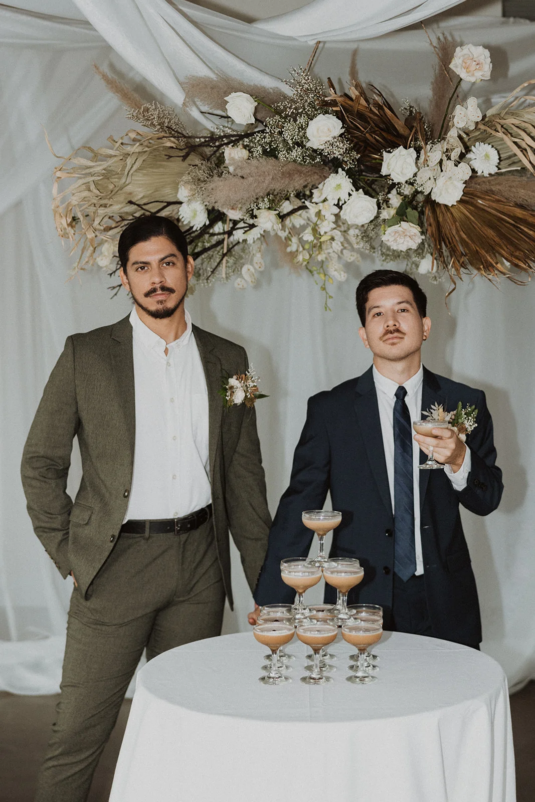 Elegant dried floral arrangement with white roses and greenery above a table with champagne glasses at a luxury wedding on Oʻahu.