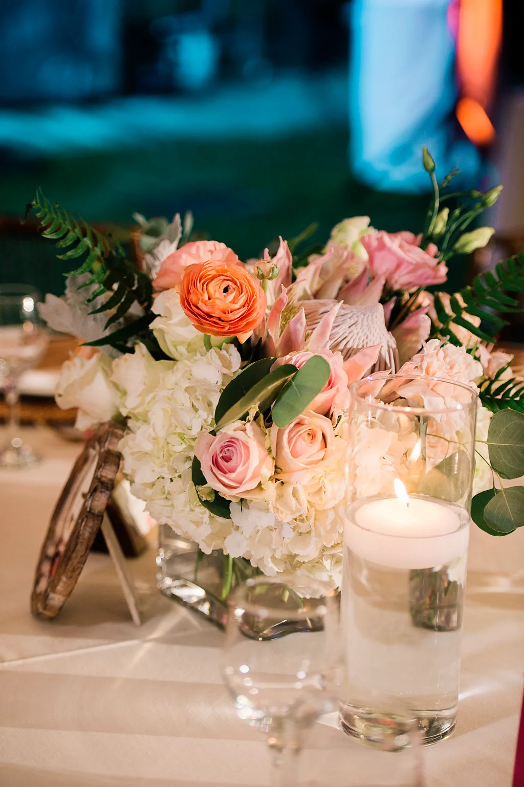 Elegant table centerpiece with pink roses, white hydrangeas, orange ranunculus, and candle at an Oʻahu wedding.