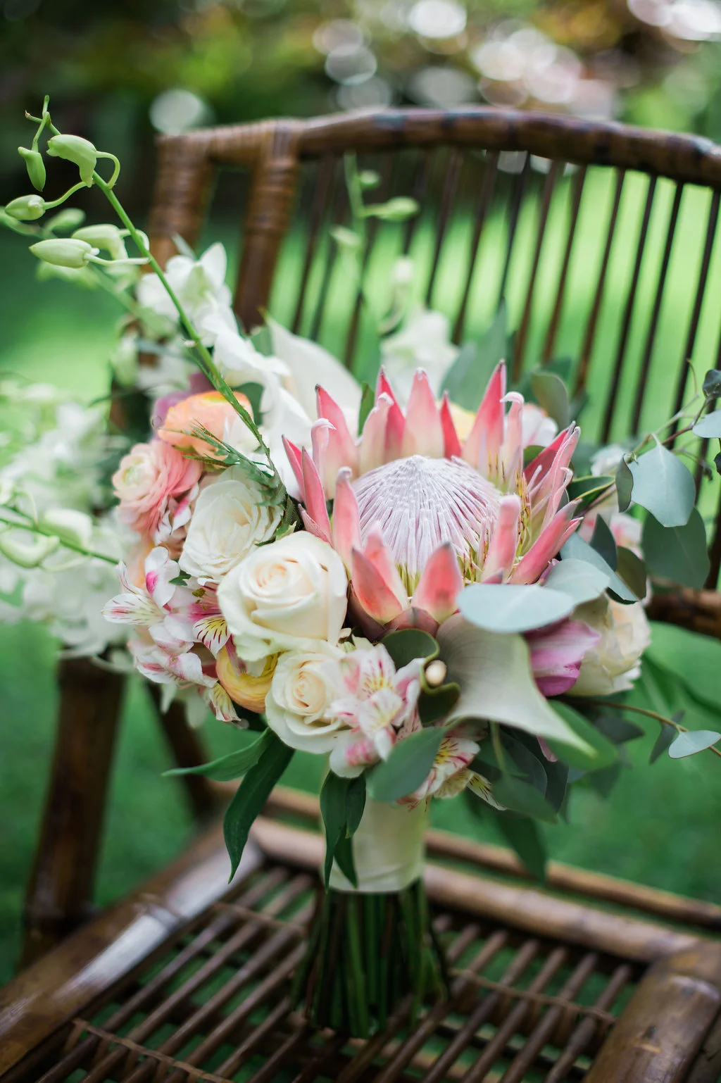 Elegant wedding bouquet with pink protea, white roses, and lush greenery on wooden chair, Oʻahu venue