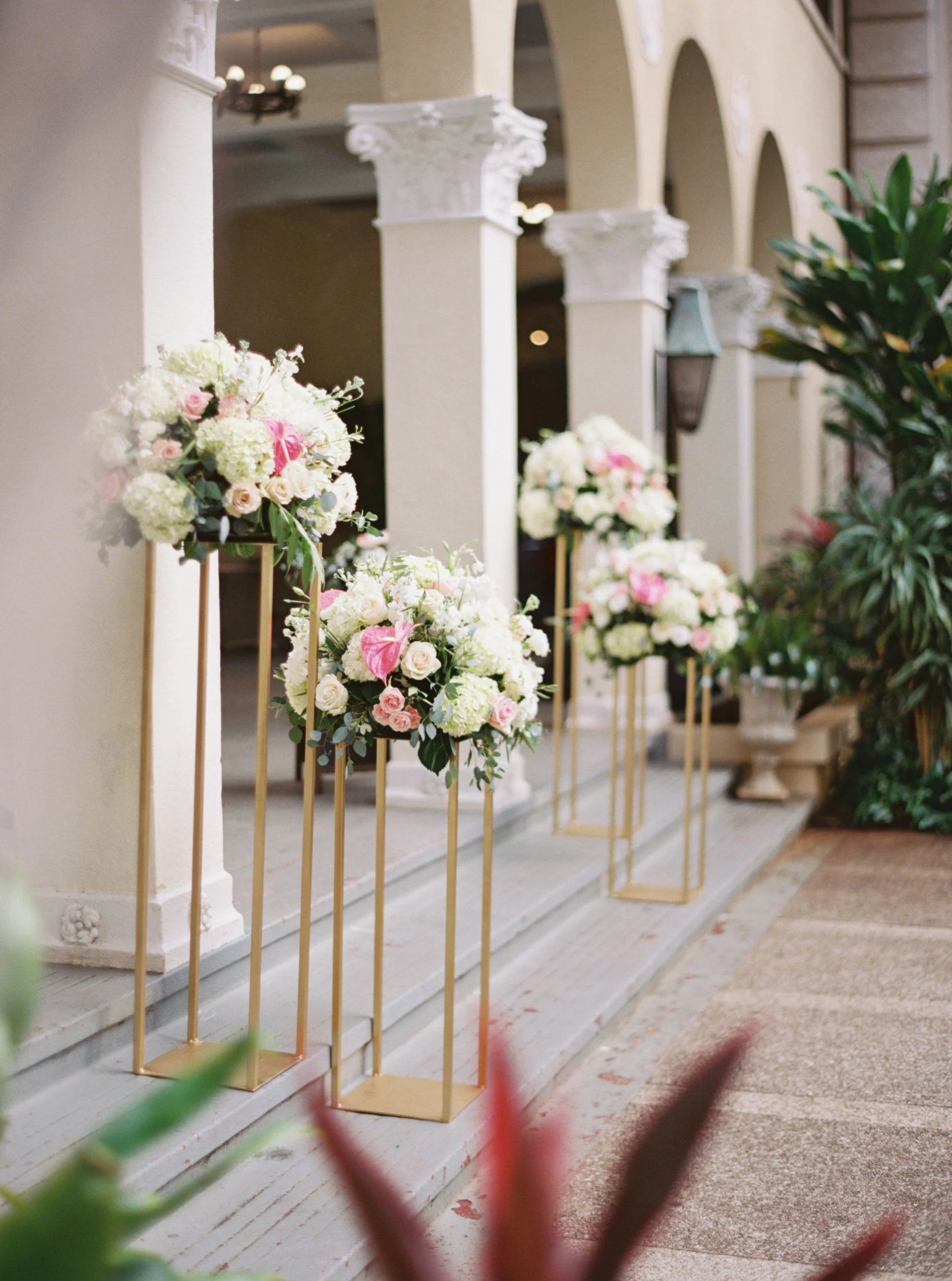 Elegant wedding florals with white and pink roses on tall gold stands at Cafe Julia, Oʻahu.