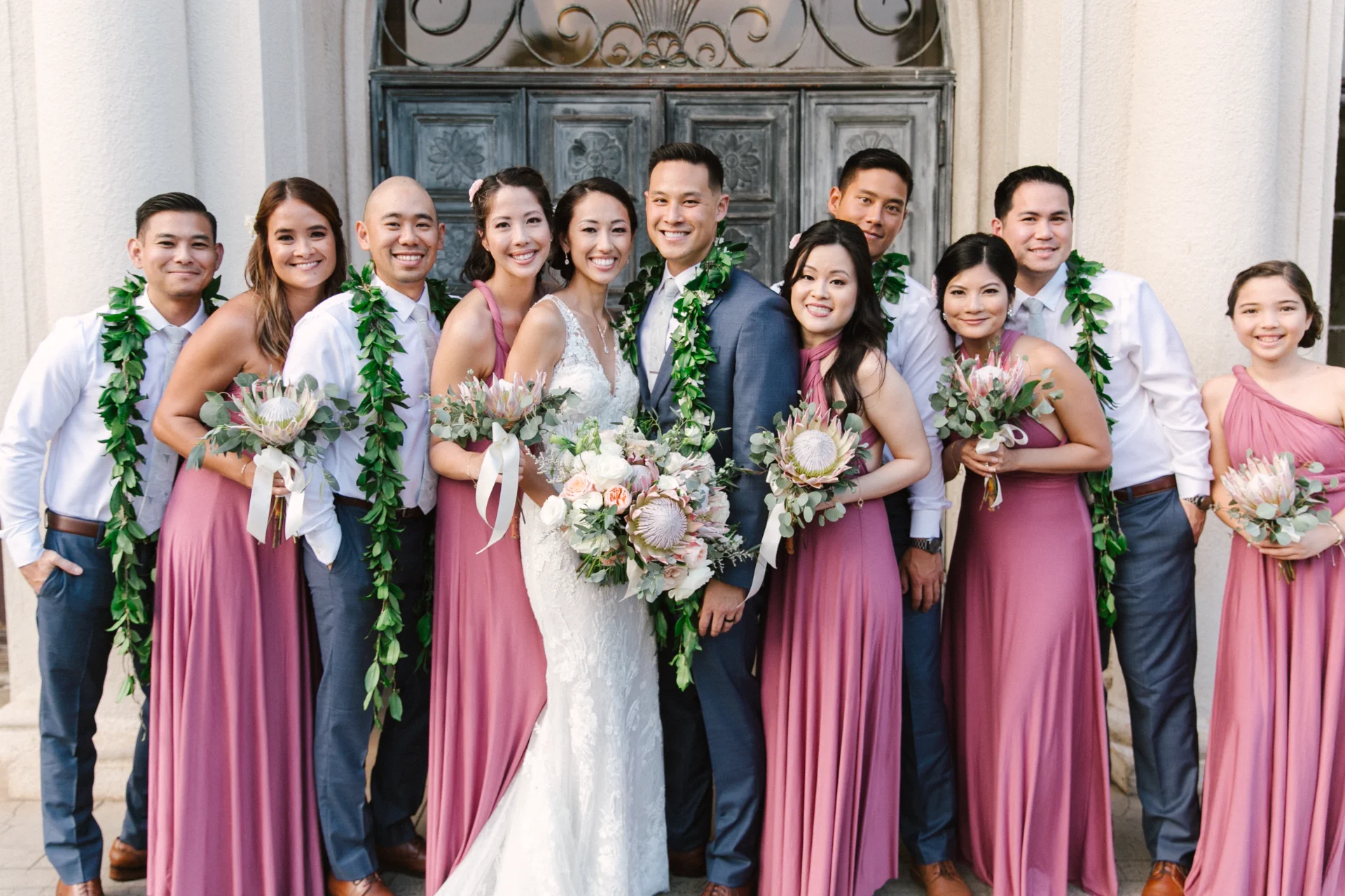 Wedding party at Cafe Julia with pink dresses, greenery leis, and protea bouquets on Oʻahu.