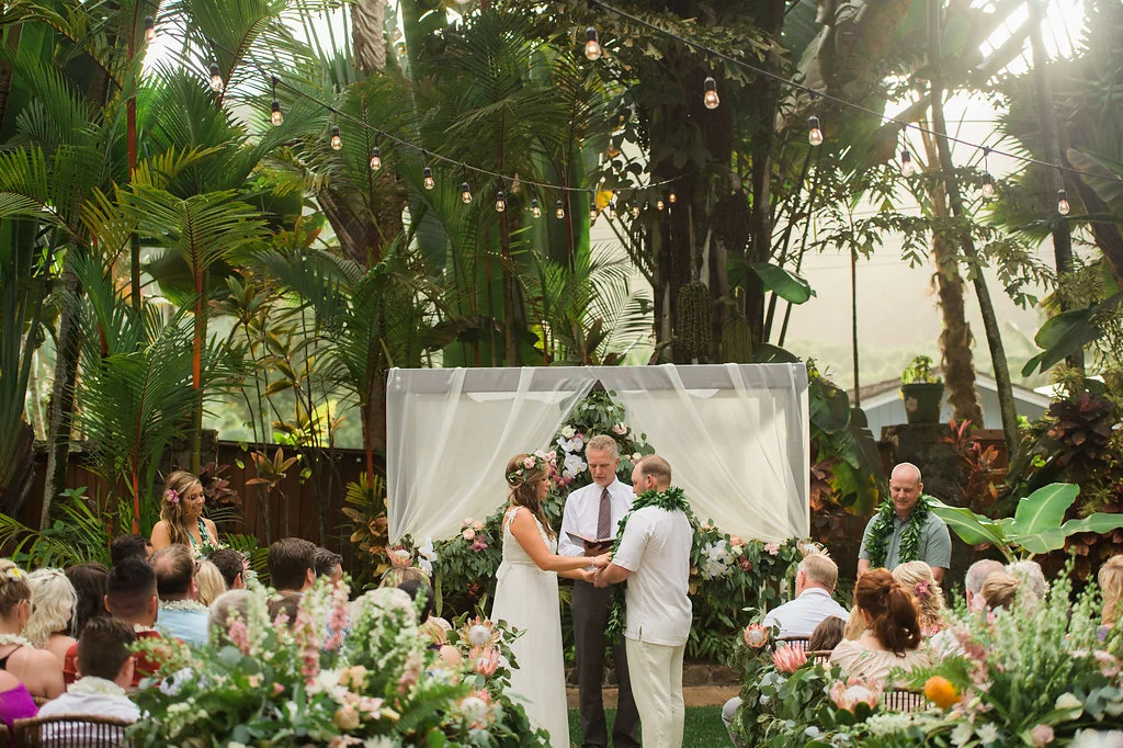 Tropical garden wedding ceremony on Oʻahu with lush greenery, pink and white floral arrangements, and an intimate gathering.