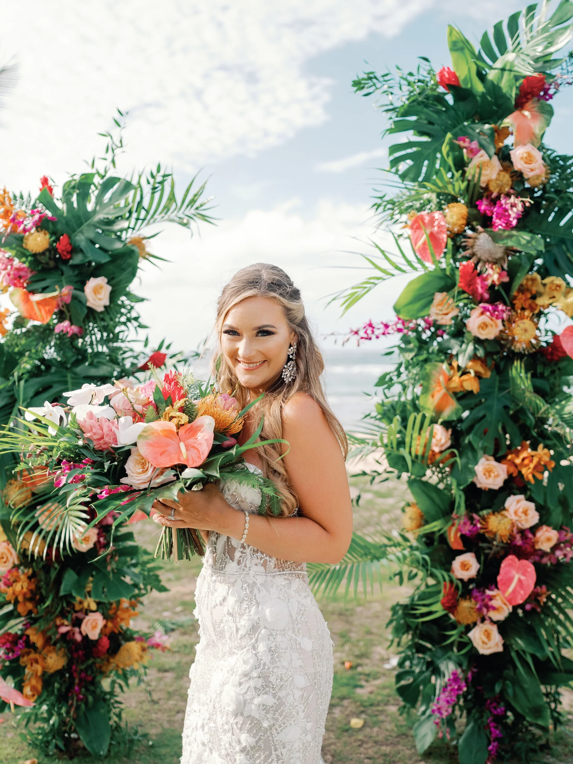 Bride holding tropical bouquet with anthuriums and roses, surrounded by lush floral arch at Loulu Palms, Oʻahu beachside. — Wedding Event Oahu Hawaii Florals Flowers Florist Creative Concepts by Jeff Alencastre