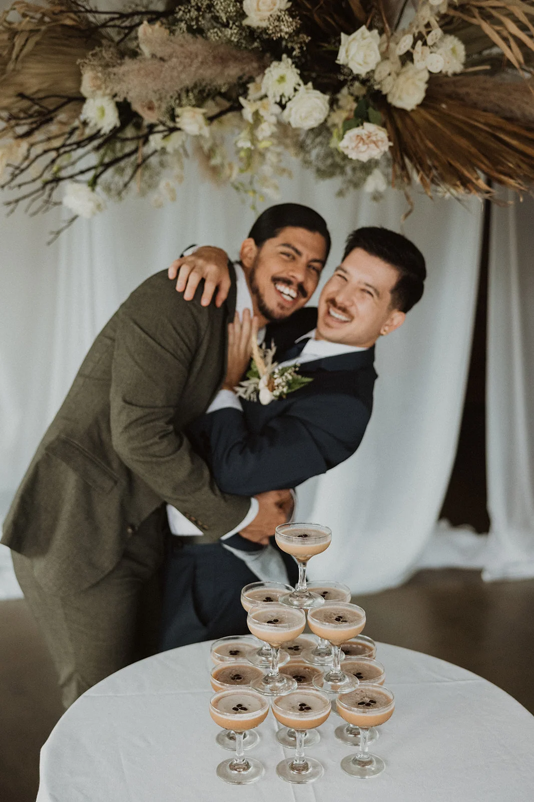 Elegant wedding floral installation in Oʻahu featuring cream roses, dried palm leaves, and pampas grass with a champagne tower.