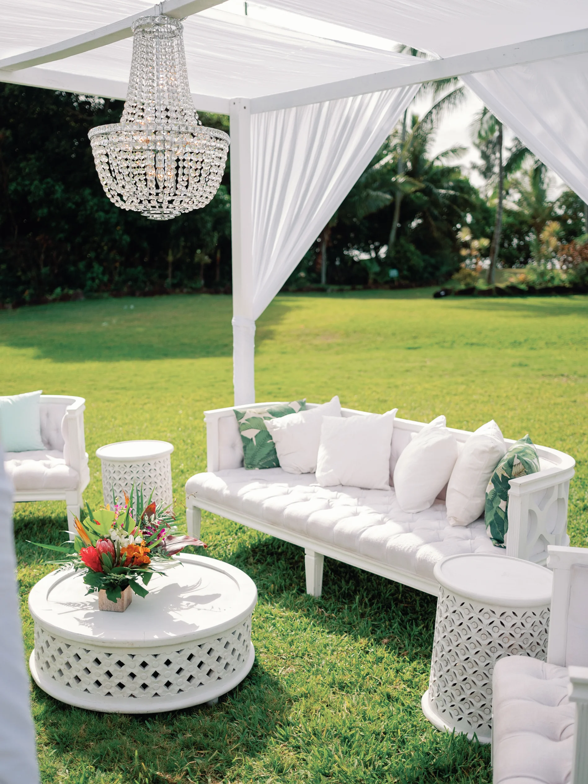 Elegant outdoor wedding lounge setup at Loulu Palms, Oʻahu, featuring white furniture, chandelier, and tropical floral arrangement. — Wedding Event Oahu Hawaii Florals Flowers Florist Creative Concepts by Jeff Alencastre