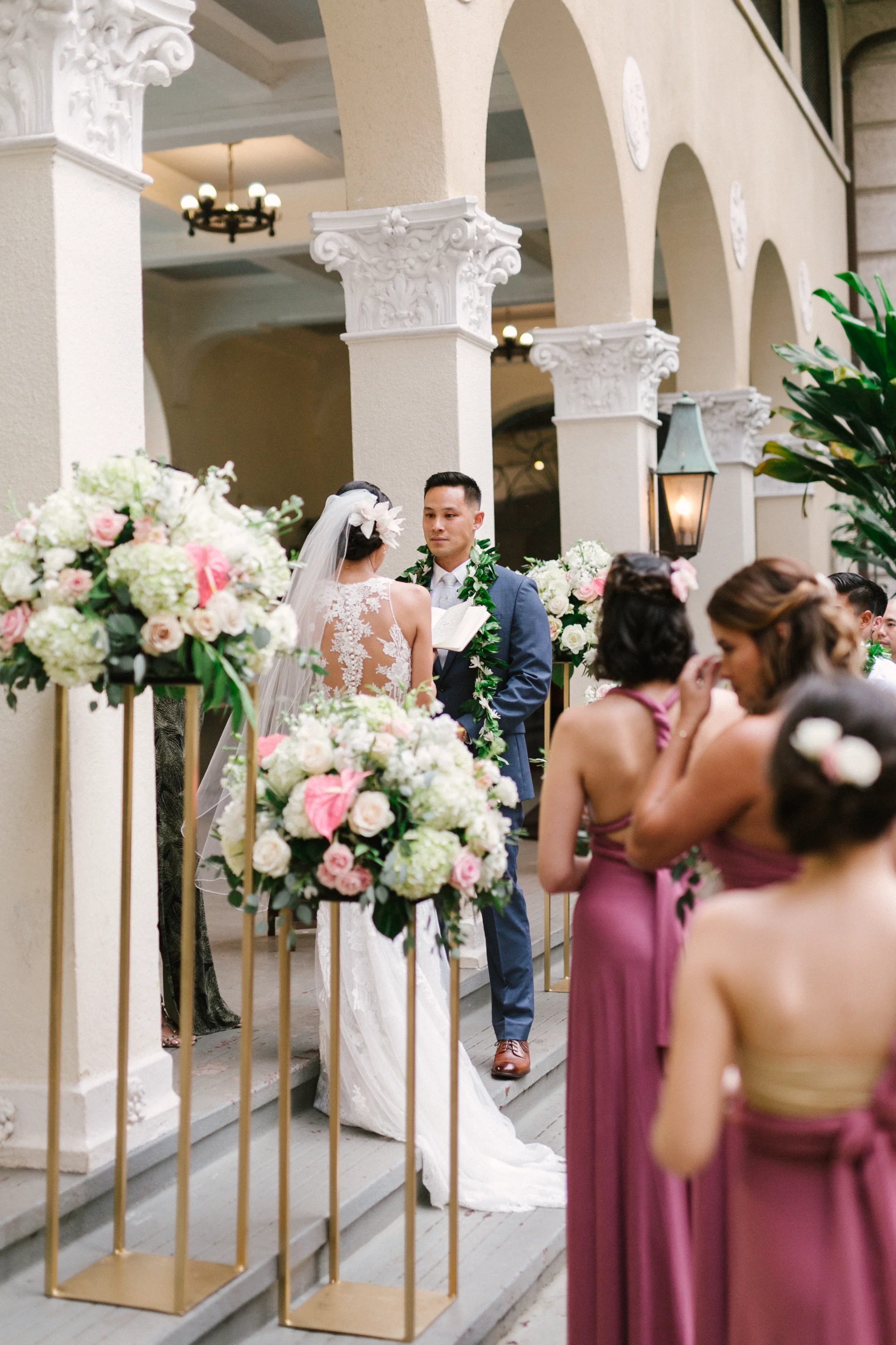 elegant wedding ceremony at Cafe Julia Oʻahu with bride, groom, and bridesmaids, featuring lush floral arrangements with roses and hydrangeas