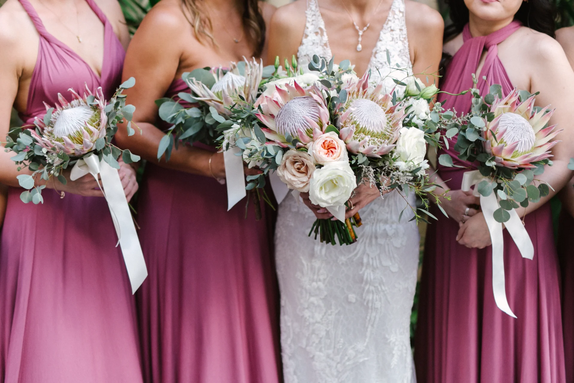 bride and bridesmaids holding king protea bouquets in mauve dresses at Cafe Julia in Hawaii