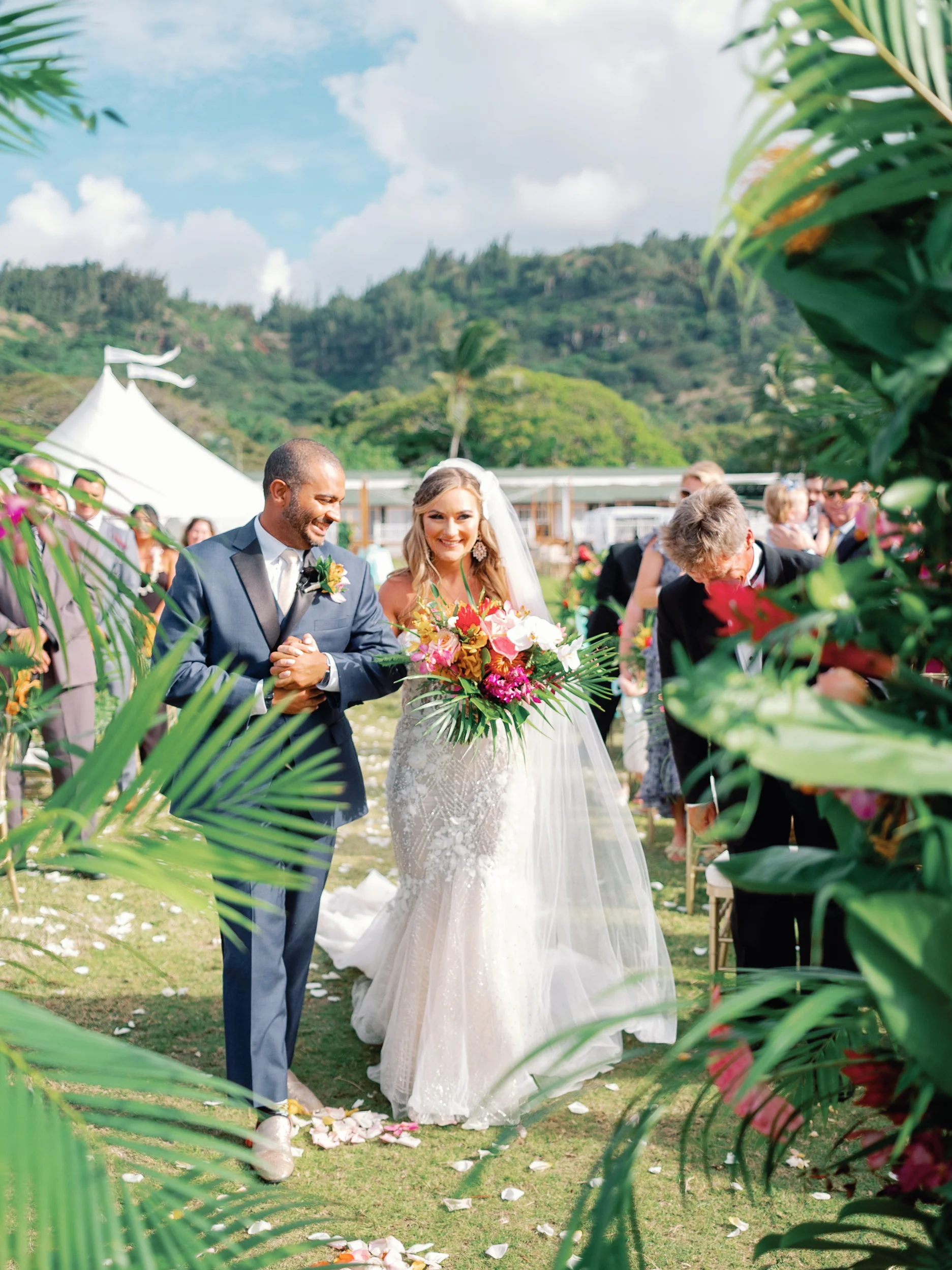 Bride with tropical bouquet and groom walking down an outdoor aisle at Loulu Palms, surrounded by palm leaves, Oʻahu. — Wedding Event Oahu Hawaii Florals Flowers Florist Creative Concepts by Jeff Alencastre