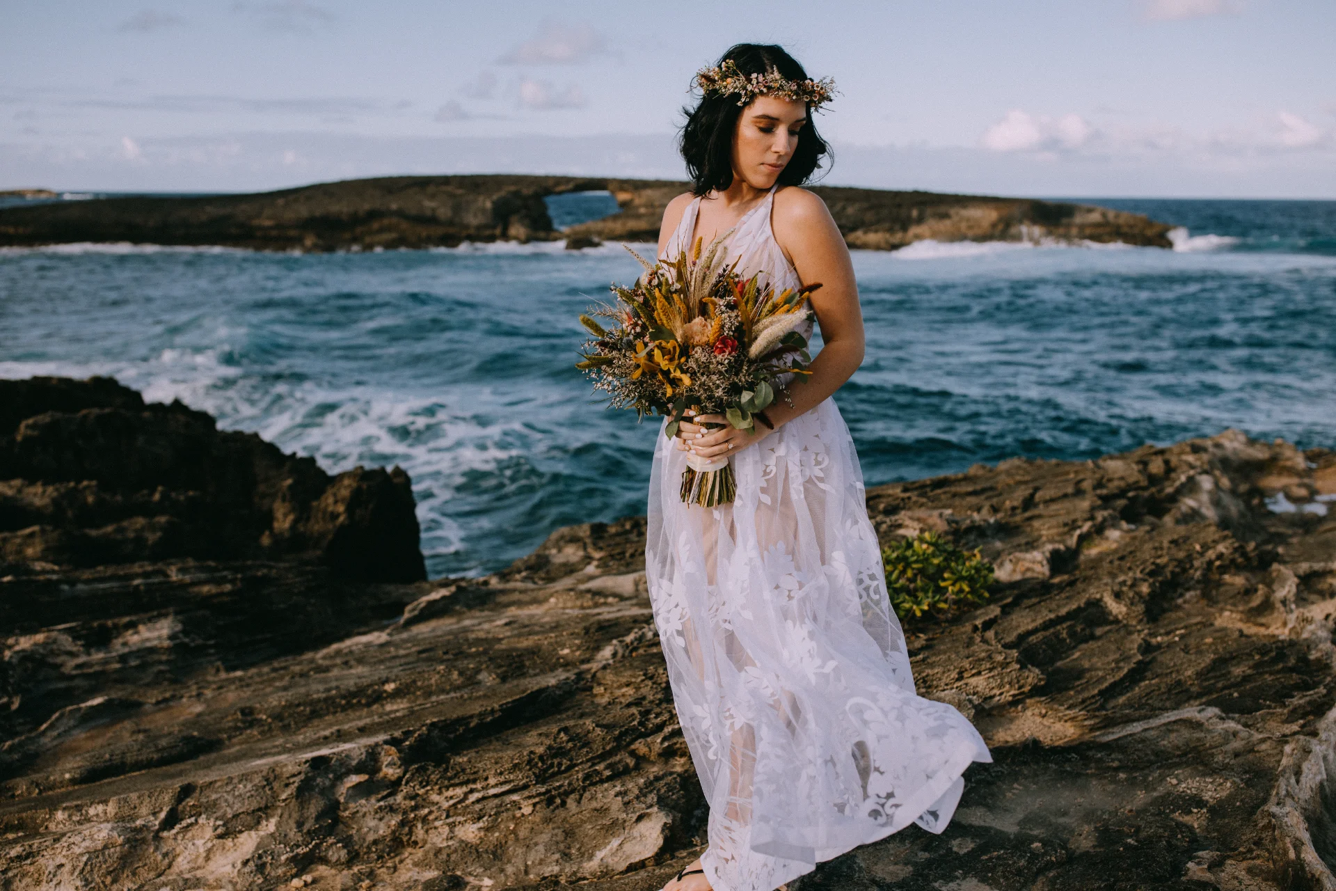Bride with tropical bouquet and floral crown on rocky Oʻahu coastline