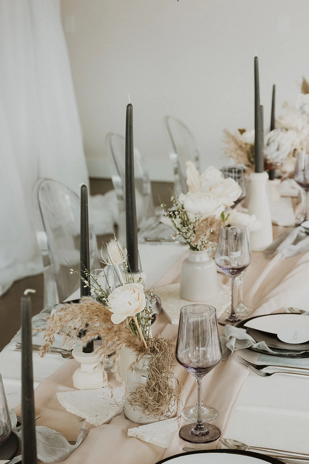 Elegant wedding table setting on Oʻahu featuring pampas grass, white roses, black candles, and sheer ghost chairs.