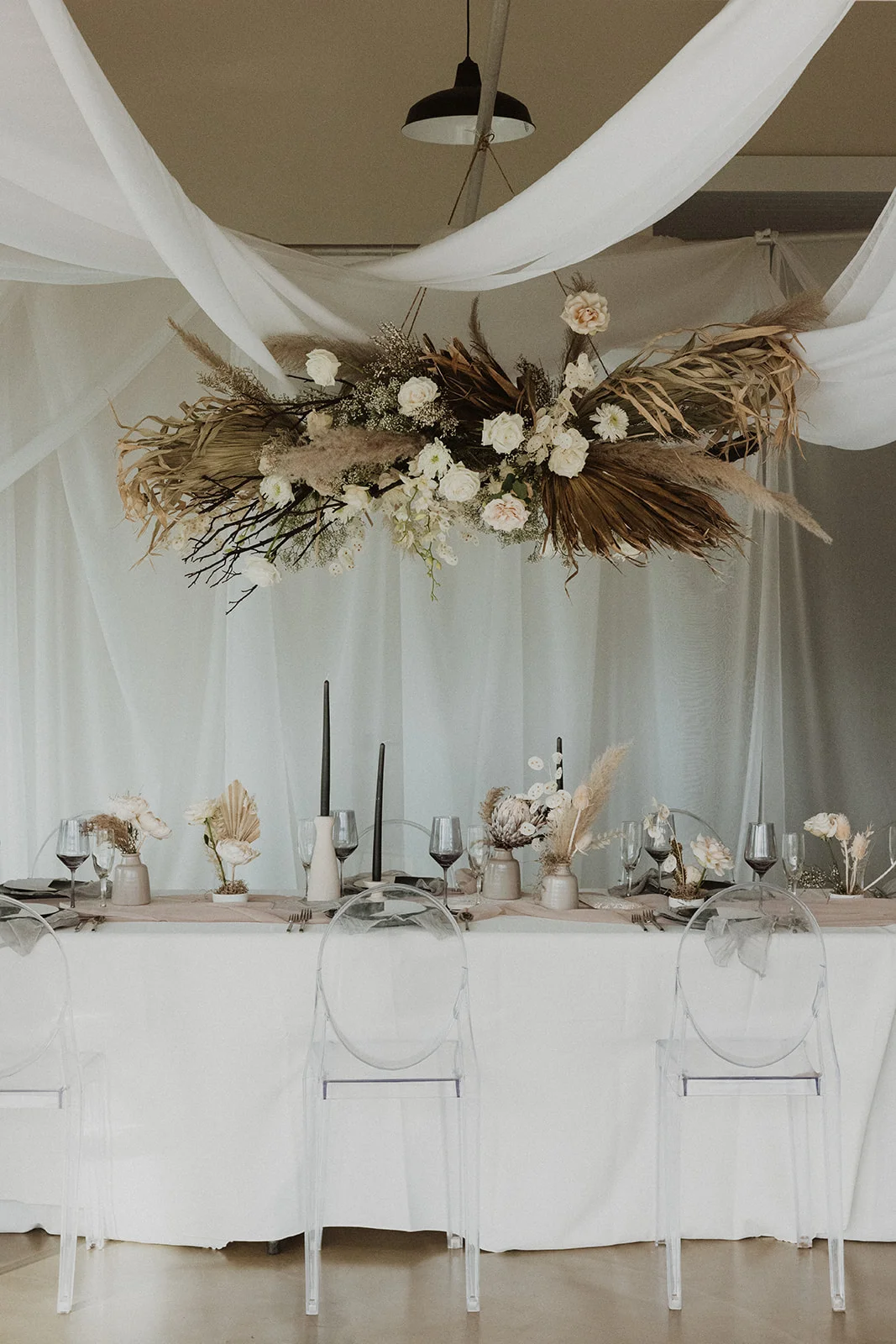 Elegant Oʻahu wedding table with hanging pampas grass and white roses, ghost chairs, and neutral florals.