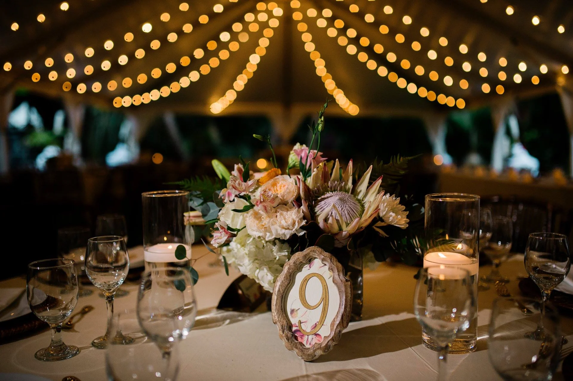 Elegant wedding table setting on Oʻahu with protea and rose centerpiece under string lights.
