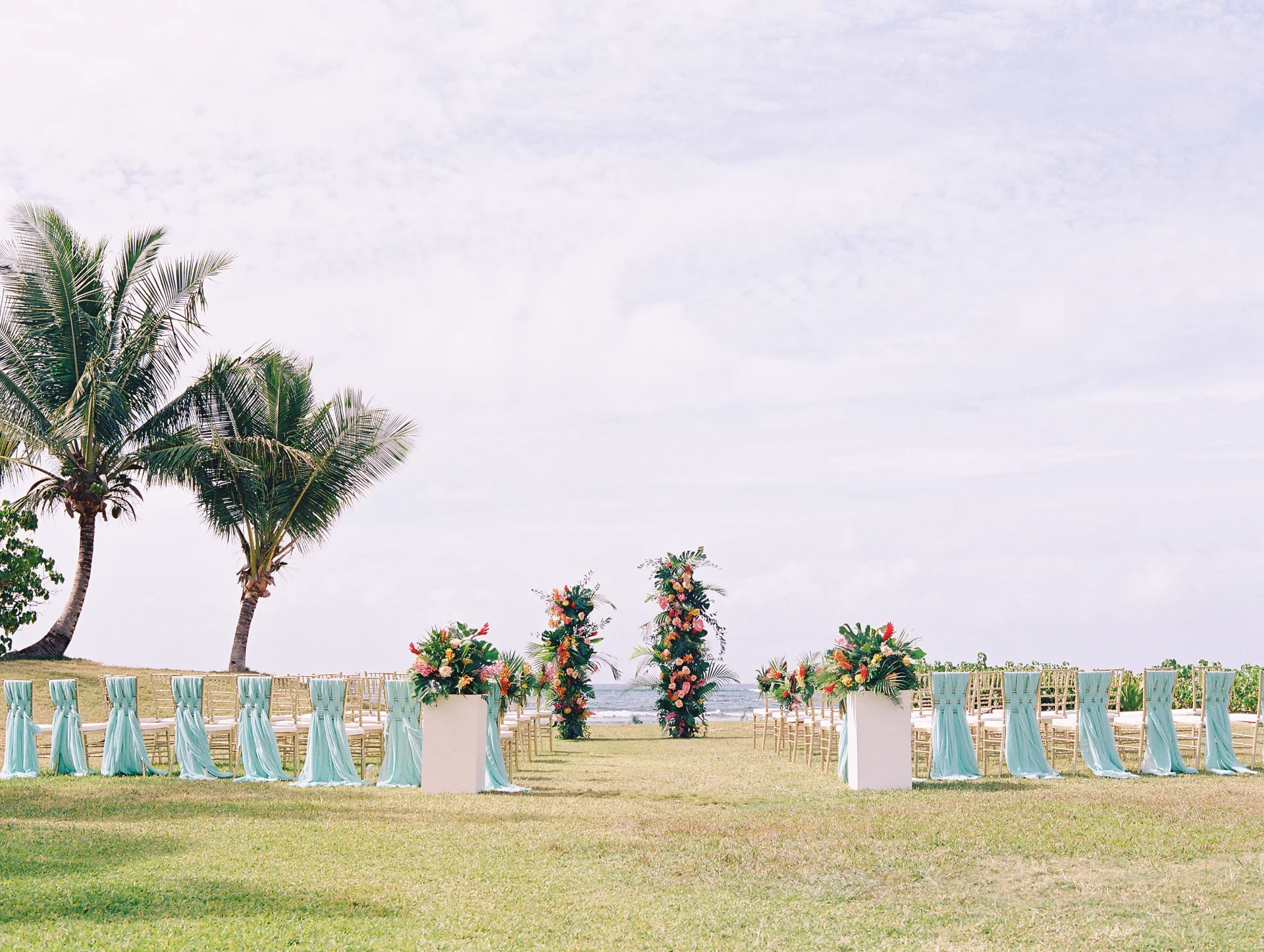Hawaii beachfront wedding ceremony setup at Loulu Palms with tropical floral arrangements and turquoise chair sashes. — Wedding Event Oahu Hawaii Florals Flowers Florist Creative Concepts by Jeff Alencastre