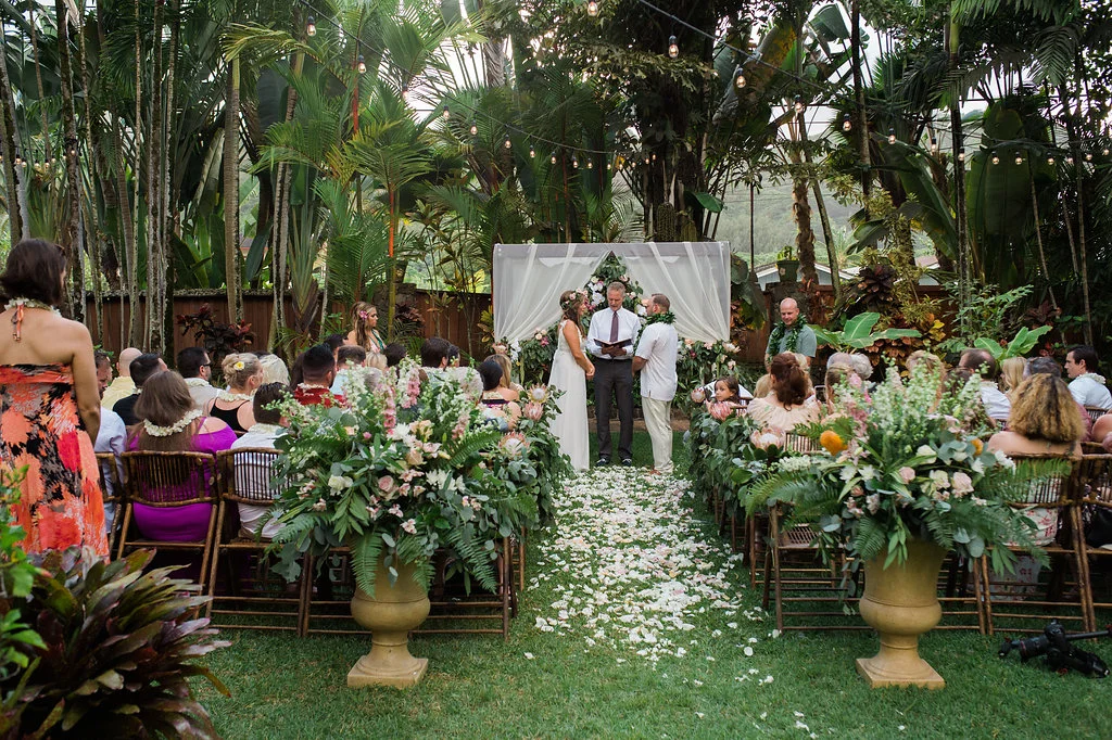 Outdoor wedding ceremony in lush Oʻahu setting, featuring elegant floral arrangements of pink and white flowers with greenery along the aisle.