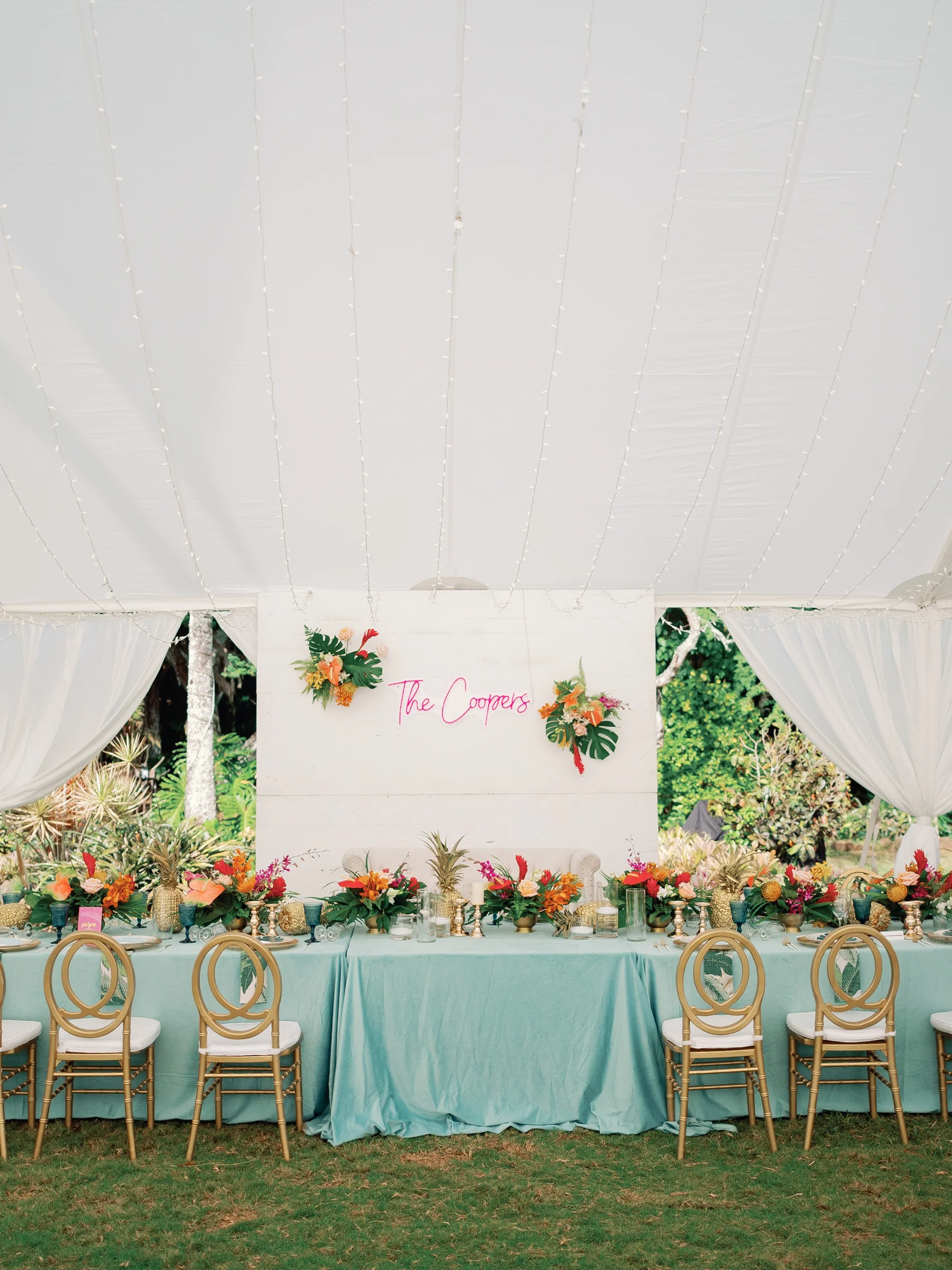 Elegant wedding reception setup at Loulu Palms, Oʻahu, with tropical floral arrangements on teal tables and gold chairs under a white tent. — Wedding Event Oahu Hawaii Florals Flowers Florist Creative Concepts by Jeff Alencastre