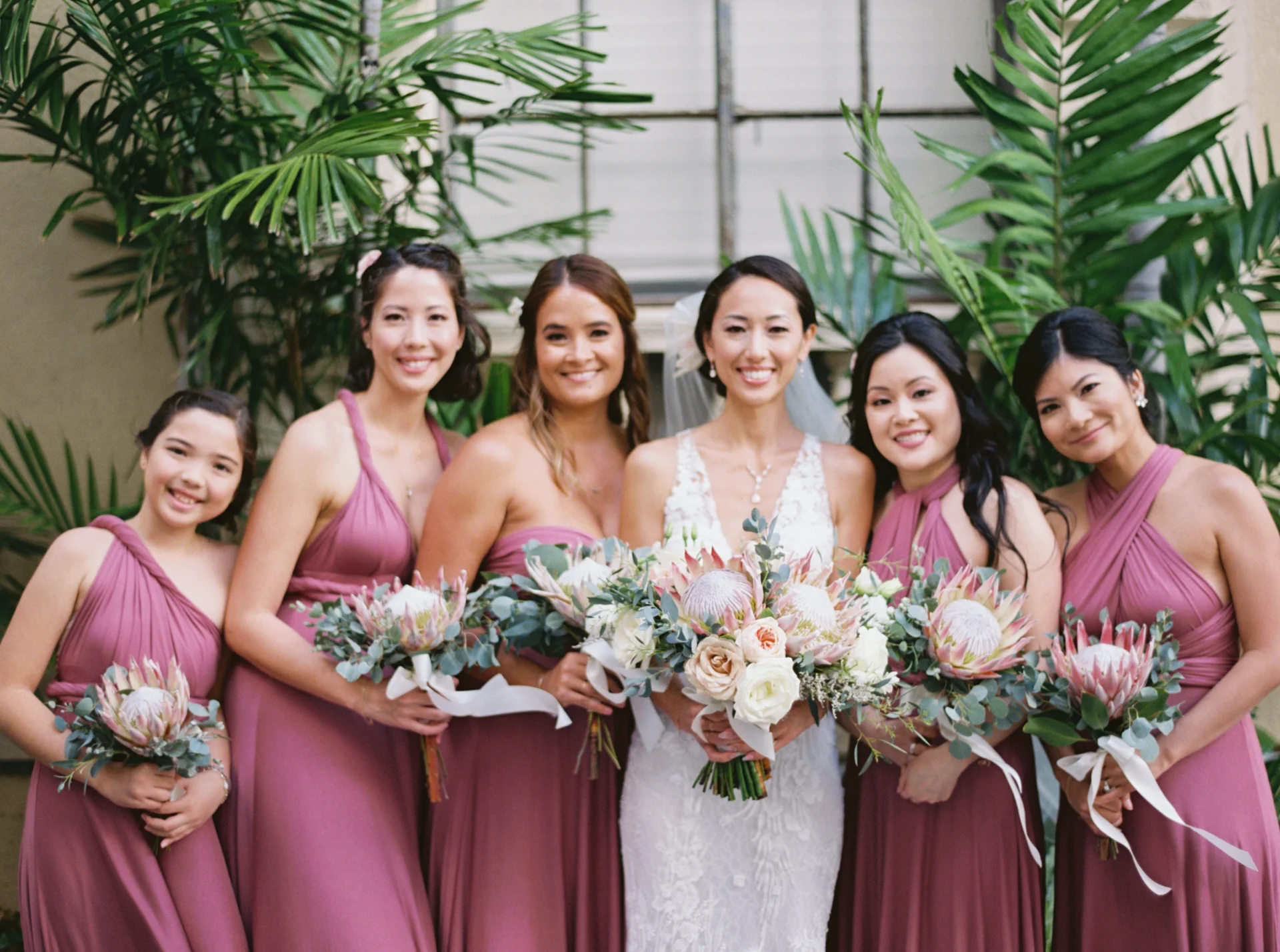 Bridesmaids in mauve dresses holding bouquets with protea flowers and eucalyptus at Cafe Julia, Oʻahu wedding