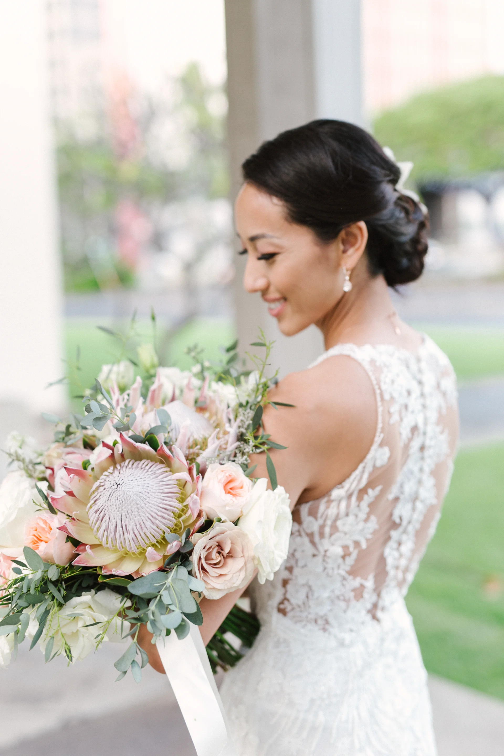 Bride holding a wedding bouquet with king protea, roses, and eucalyptus at Cafe Julia, Oʻahu.